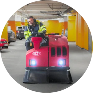 Sopmaskinist kör en röd städmaskin i parkeringsgarage – PL Utemiljö utför professionell garagestädning.