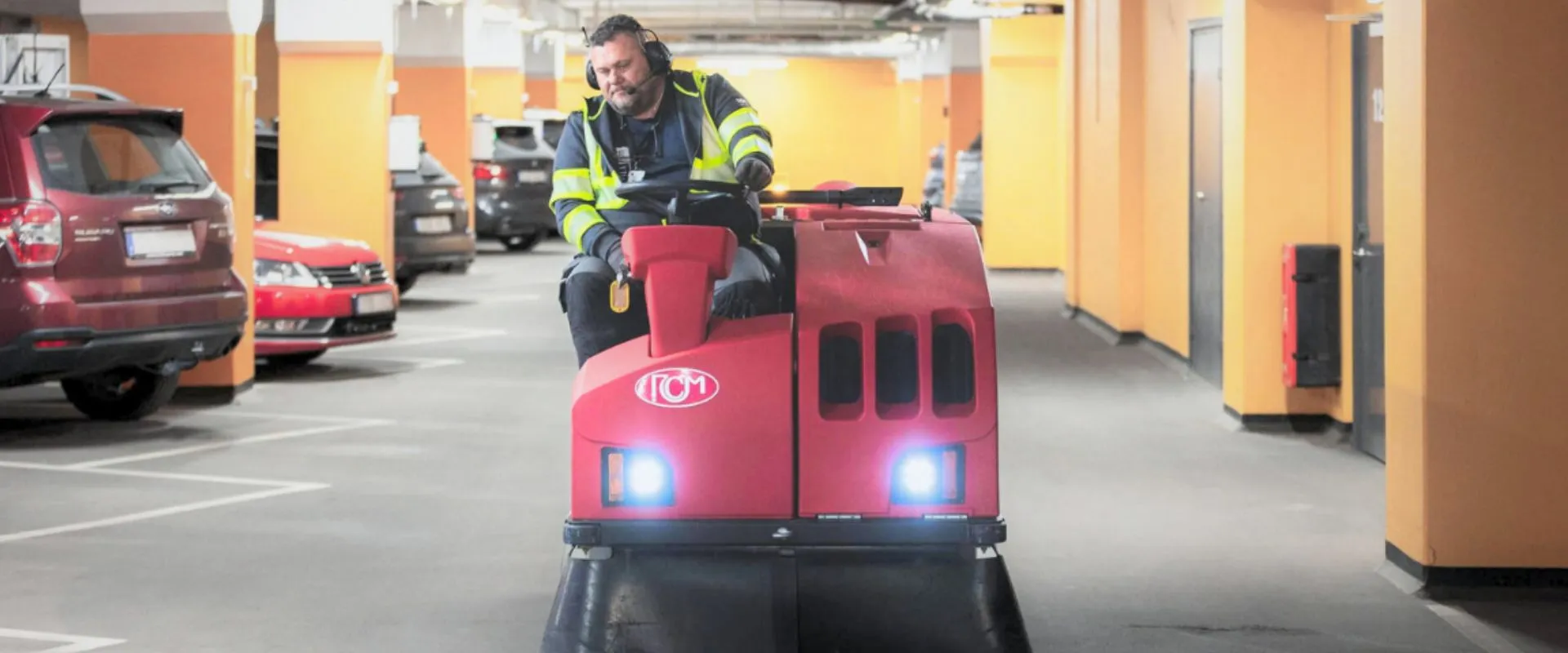 Medarbetare kör en sopmaskin i ett parkeringsgarage – professionell garagestädning för rena och säkra inomhusmiljöer.
