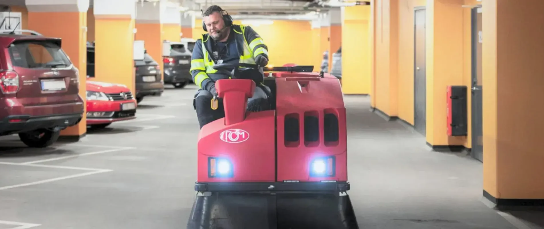 Medarbetare kör en sopmaskin i ett parkeringsgarage – professionell garagestädning för rena och säkra inomhusmiljöer.
