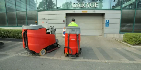 Två röda städmaskiner och en person i arbetskläder framför en garageport till ett parkeringsgarage
